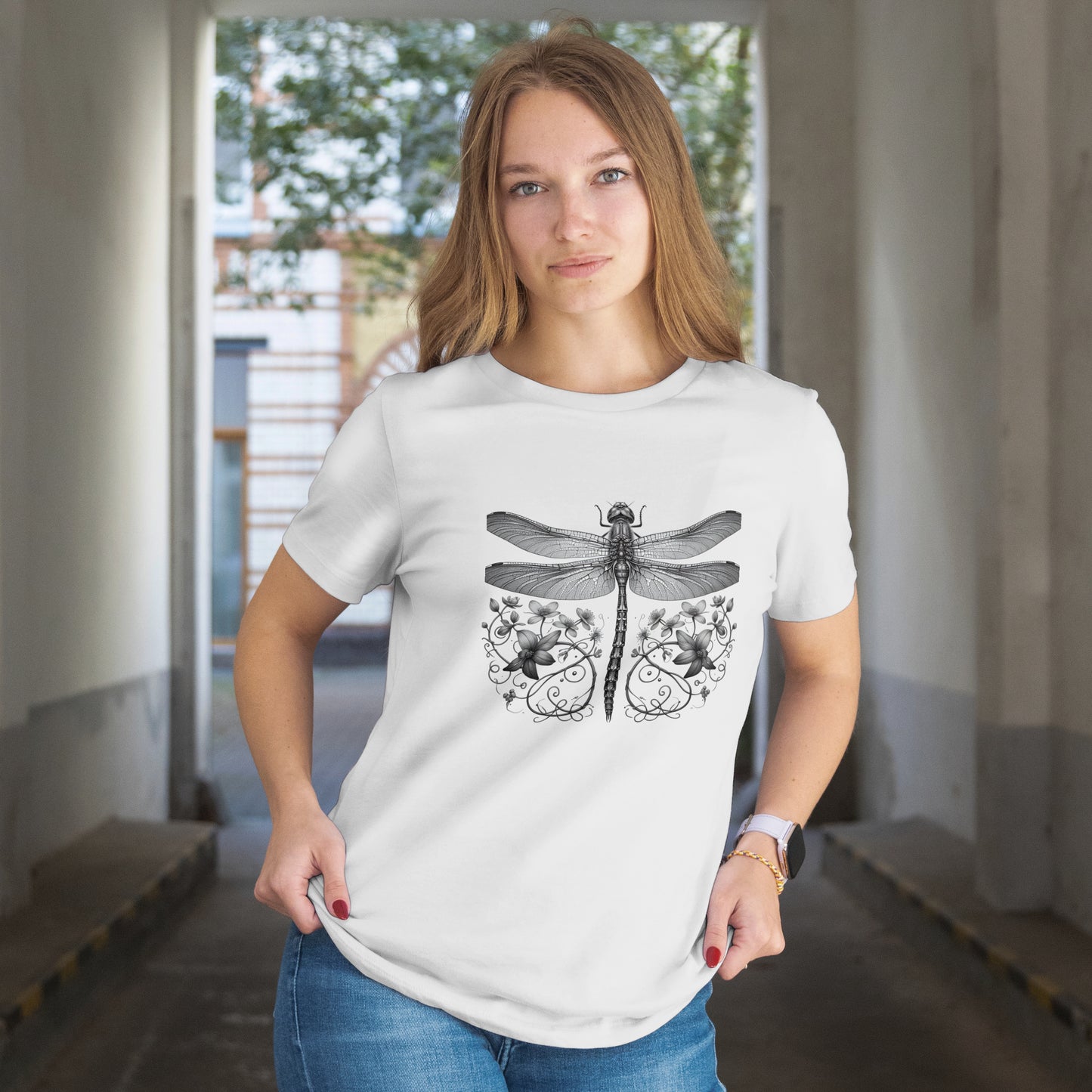 Woman wearing a white t-shirt with a Black and white illustration of a dragonfly with floral elements on a white background. The model is in an indoor setting.