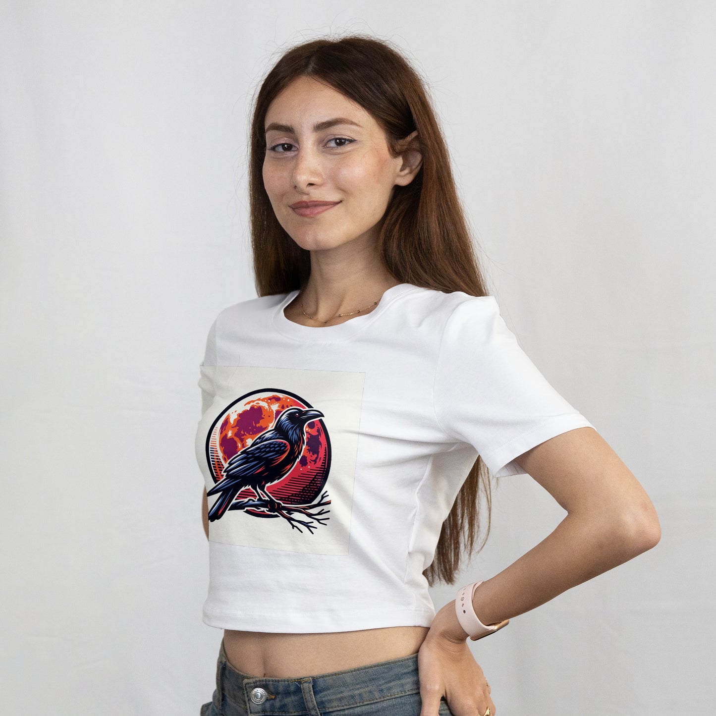 Woman standing with her hands on her hips wearing a white t-shirt with a Black crow perched on a branch with an orange and red moon in the background