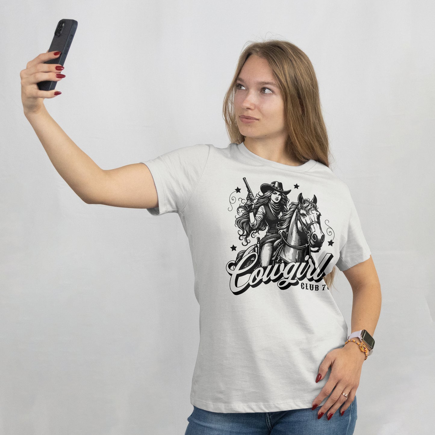 Woman wearing a white t-shirt with a 'Black and white illustration of a cowgirl on a horse with 'Cowgirl Club 707' text. The model is standing against a plain background