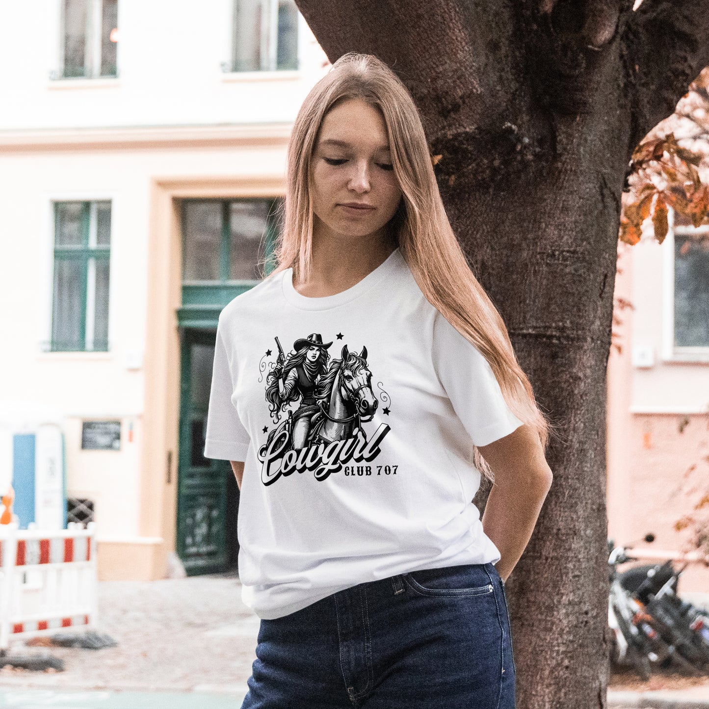 Woman wearing a white t-shirt with black and white illustration of a cowgirl on a horse with 'Cowgirl Club 707' text, standing outdoors.