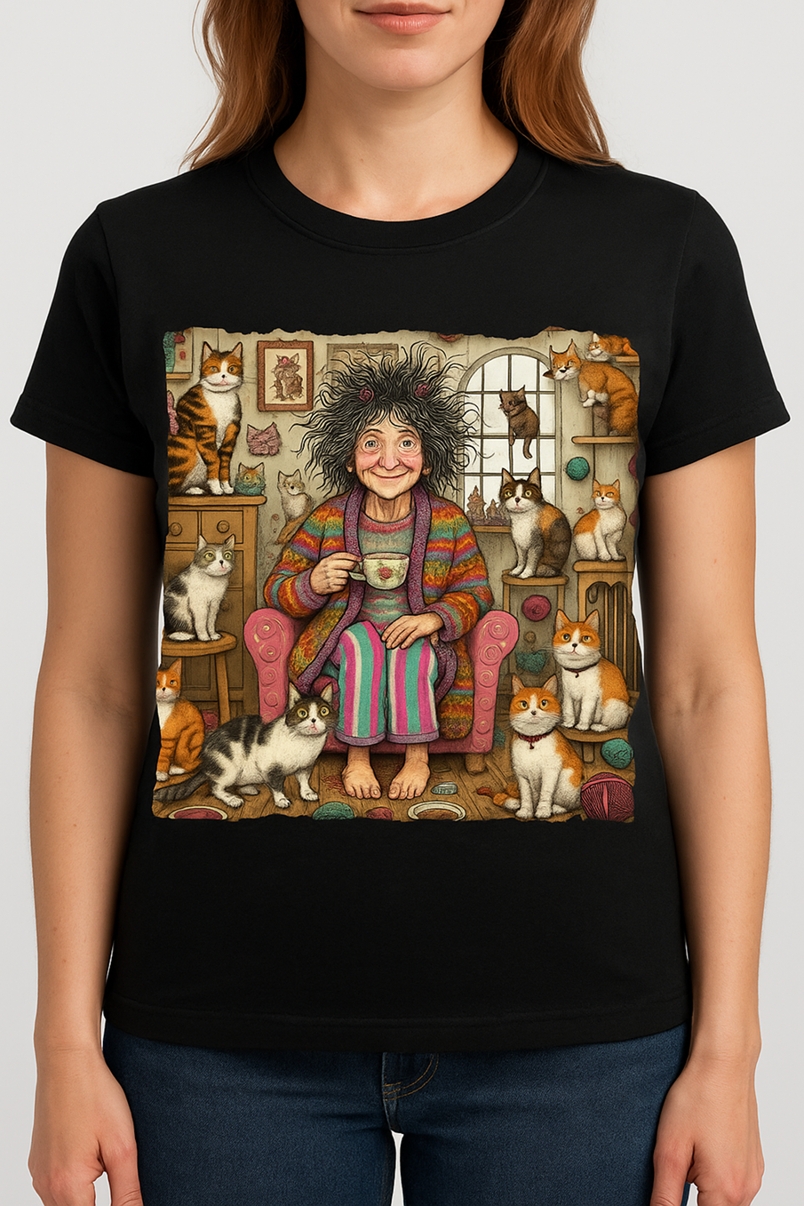 A woman in a black t-shirt with a graphic of a woman drinking a cup of coffee in a colorful robe surrounded by cats in a cozy room.