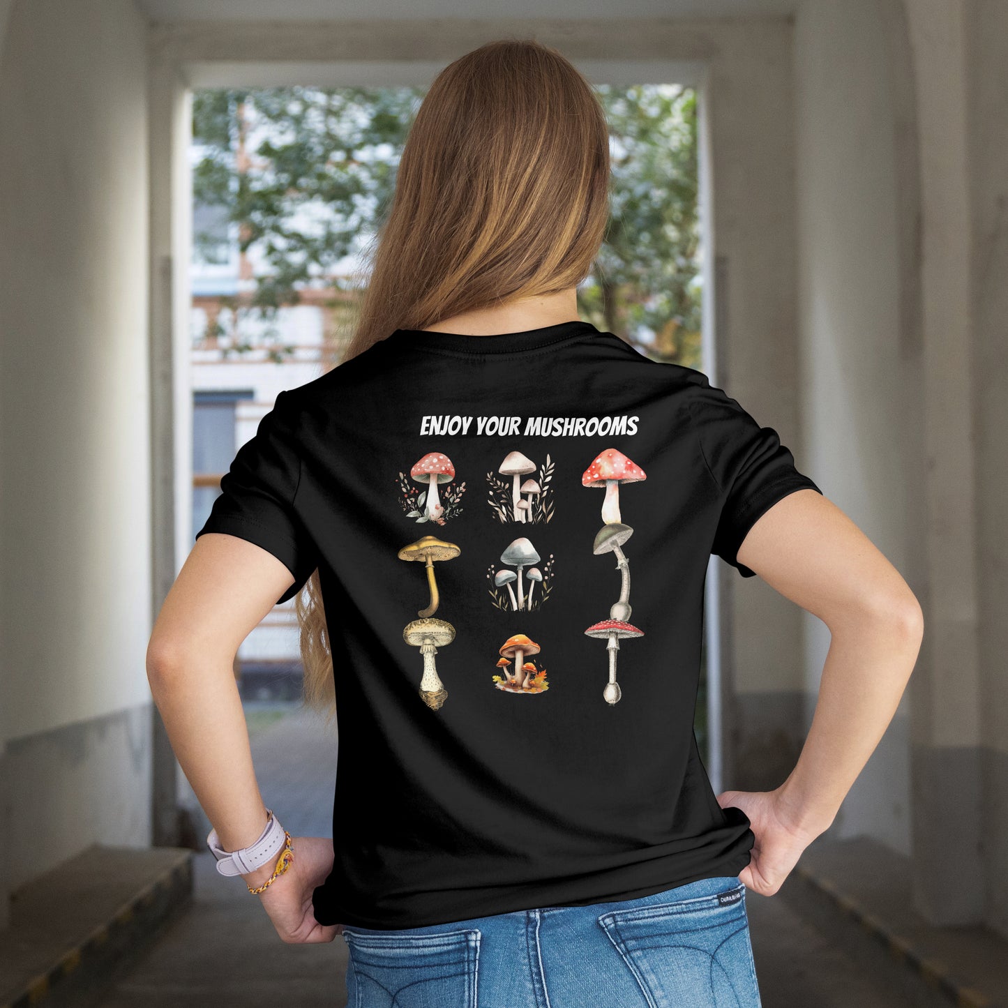 Person wearing a black t-shirt with Illustrations of various mushrooms on a white background, standing in an indoor setting.