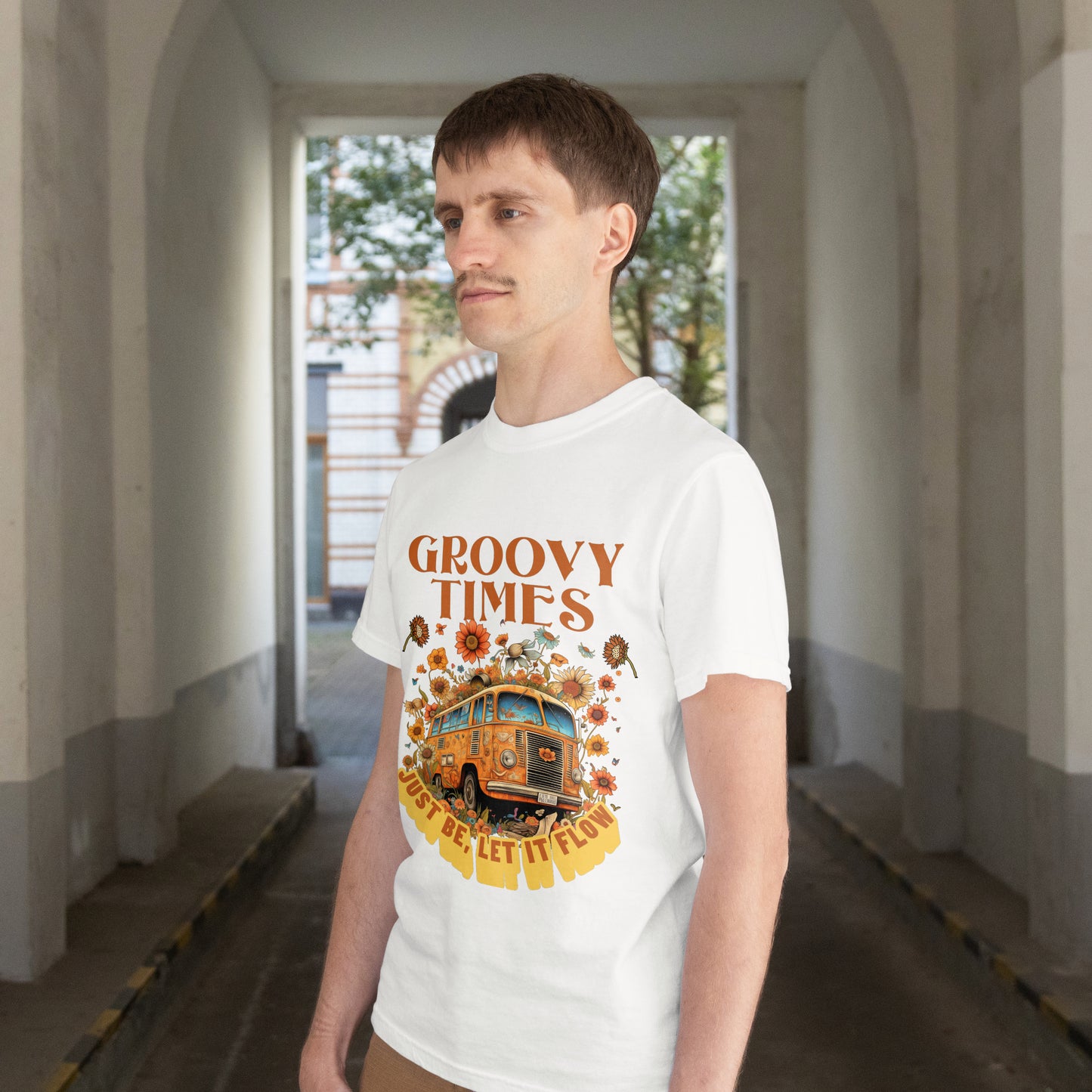 Person wearing a white t-shirt with a Vintage bus surrounded by flowers with 'Groovy Times Just Be, Let It Flow' text on a white background in an indoor setting.