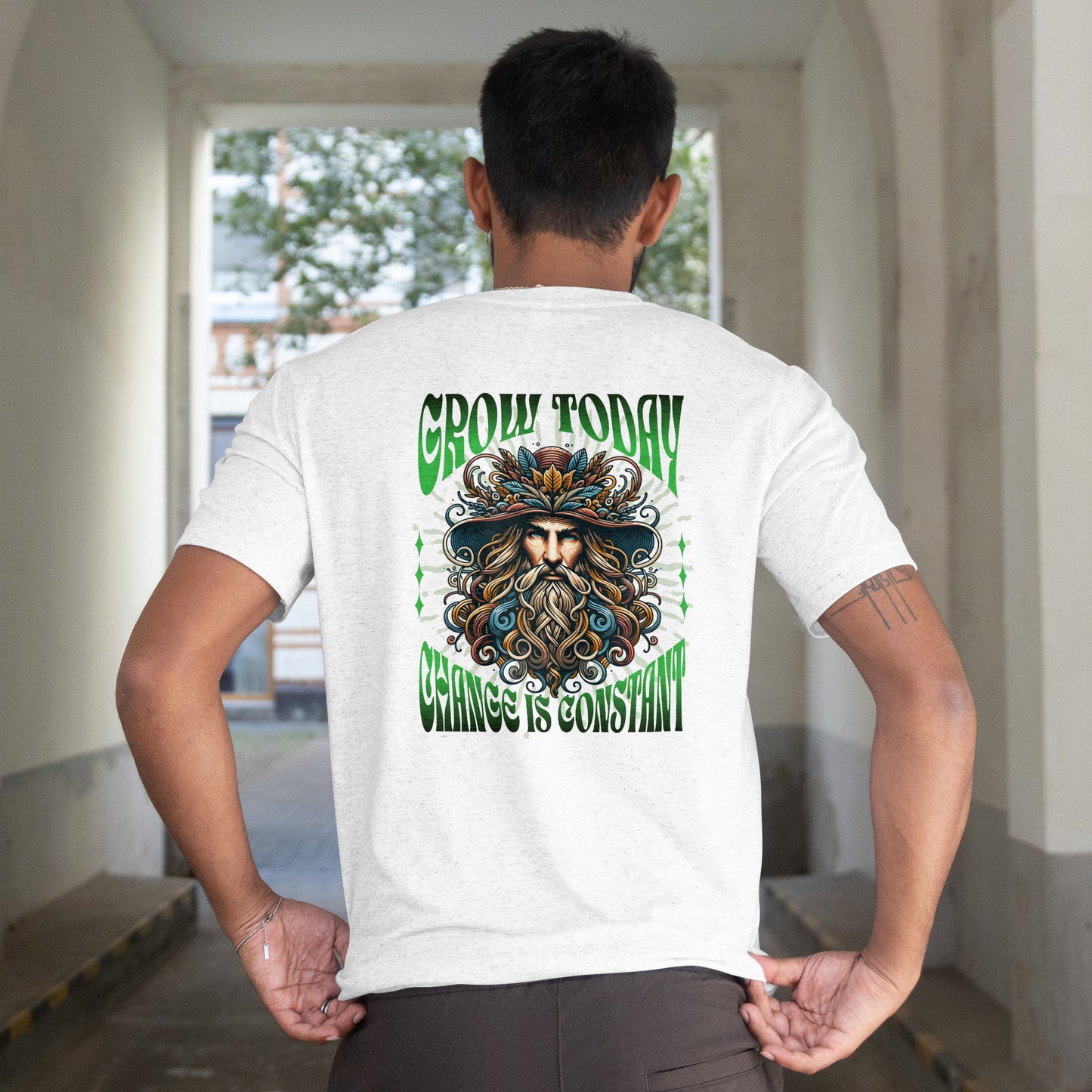 Person wearing a white t-shirt with a graphic t-shirt featuring a colorful illustration of a bearded character with a hat, set against a green and white background. on the back, standing in an indoor setting.