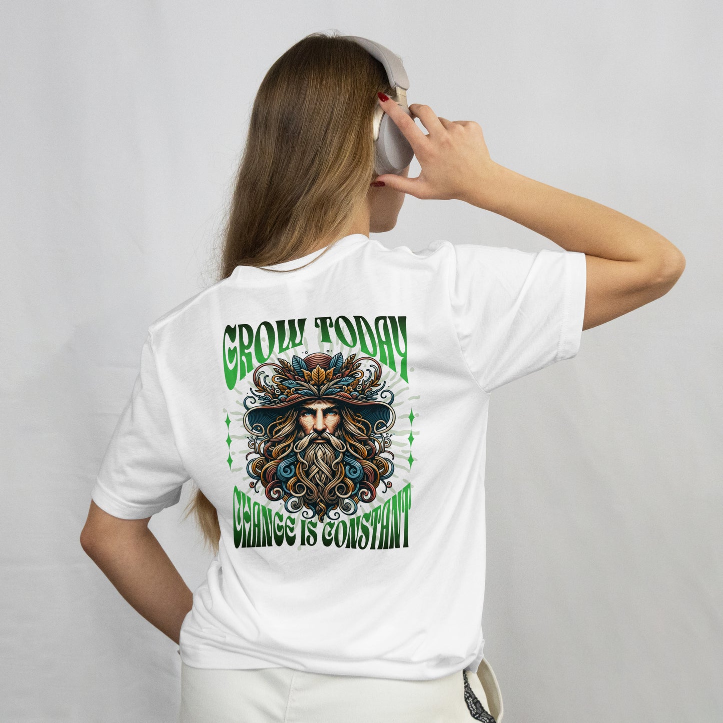 Person wearing a white t-shirt with a A graphic t-shirt featuring a colorful illustration of a bearded character with a hat, set against a green and white background, against a plain background.