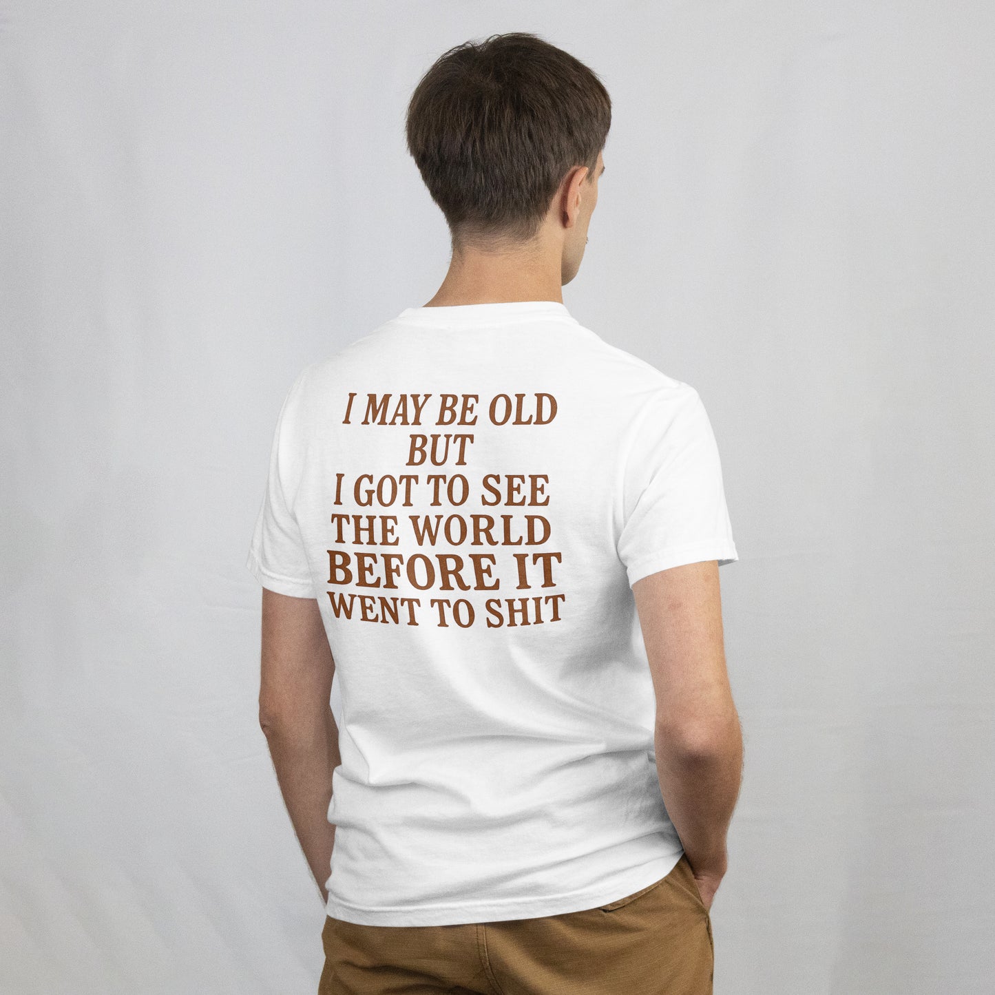 Person wearing a white t-shirt with "I may be old but I got to see the world before it went to shit" on the back against a plain background