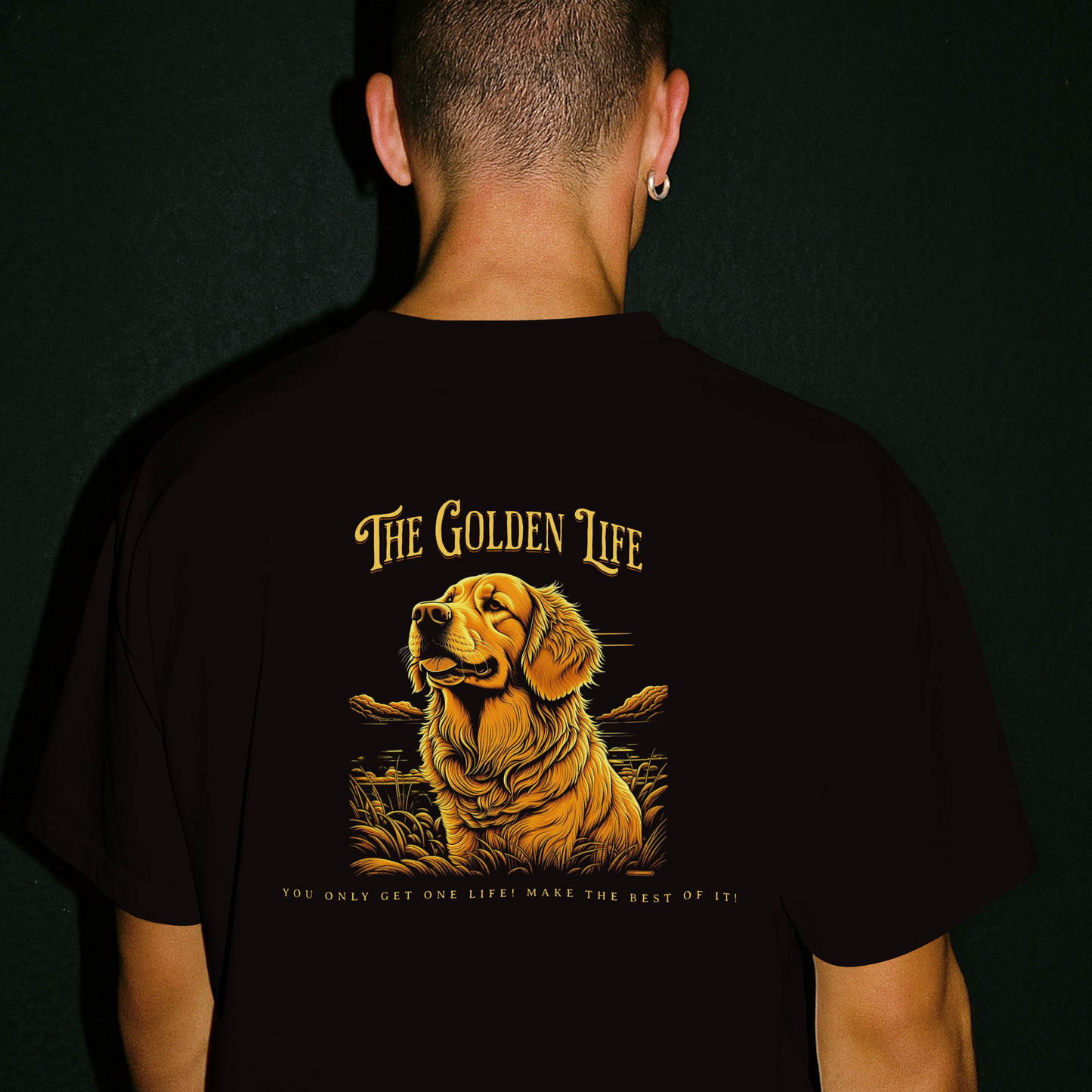 Person wearing a black t-shirt with a Illustration of a golden retriever with 'The Golden Life' text on a black background. The person is standing against a dark background.