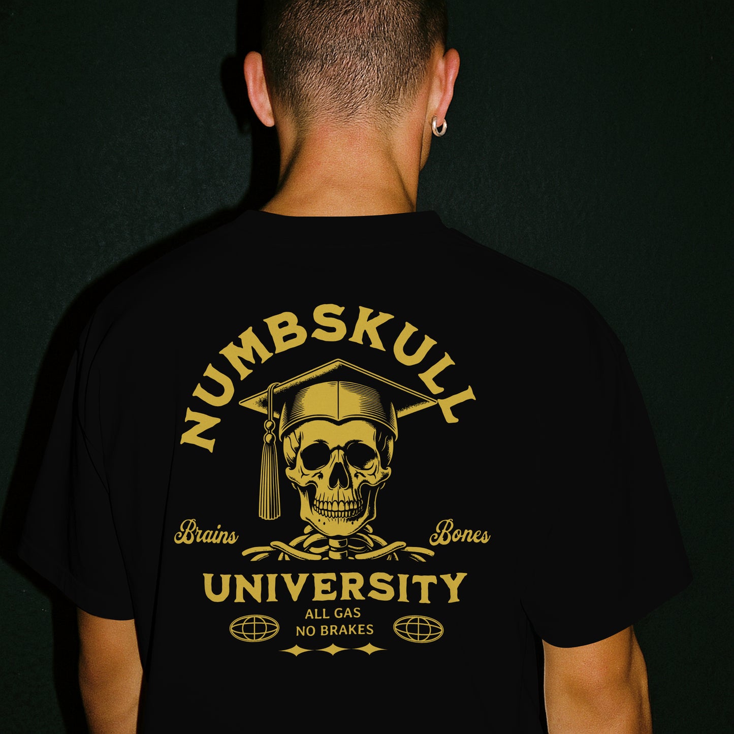 Person wearing a black t-shirt with a gold skull with graduation cap and 'Numbskull University' text on a black background on the back of the shirt.