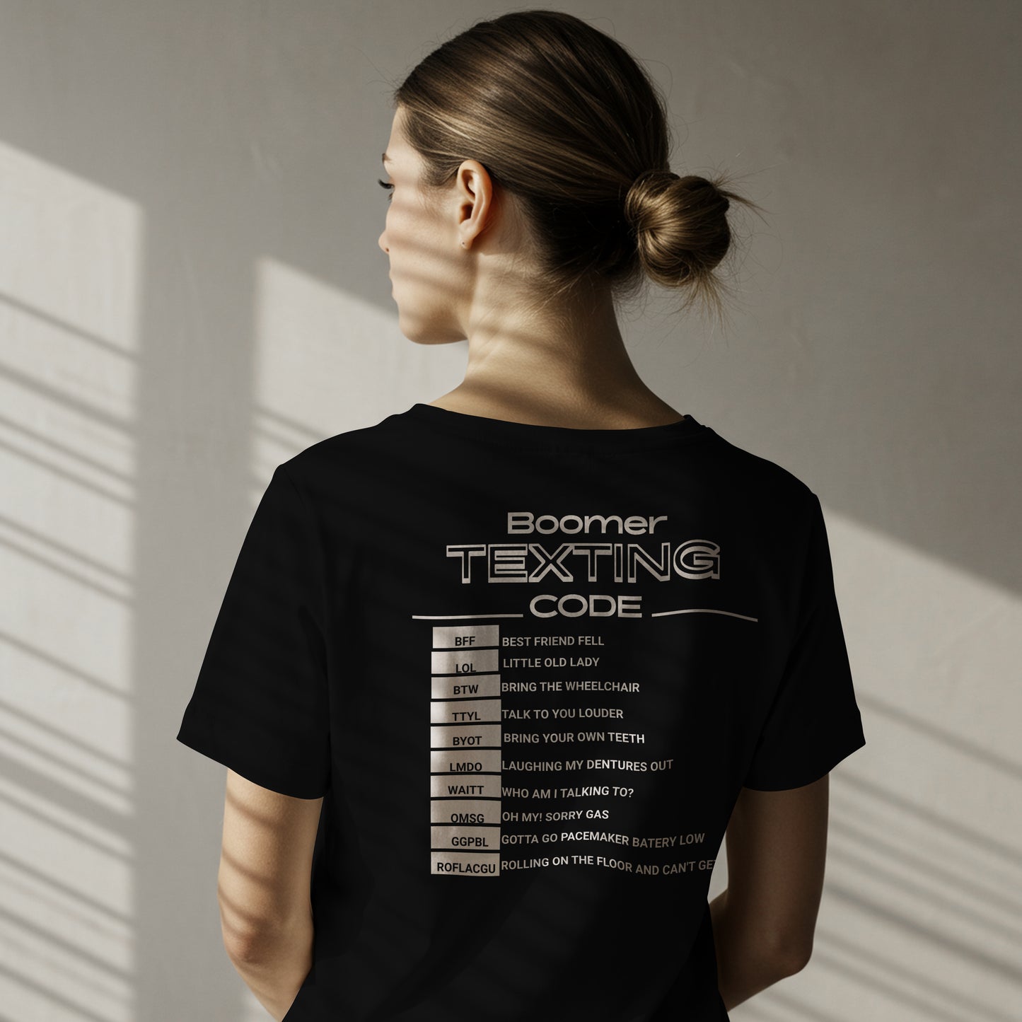 Female wearing a black t-shirt with 'Boomer Texting Code' The code consists of abbreviations and there means. The image is on the back, and the model is standing against a neutral wall.