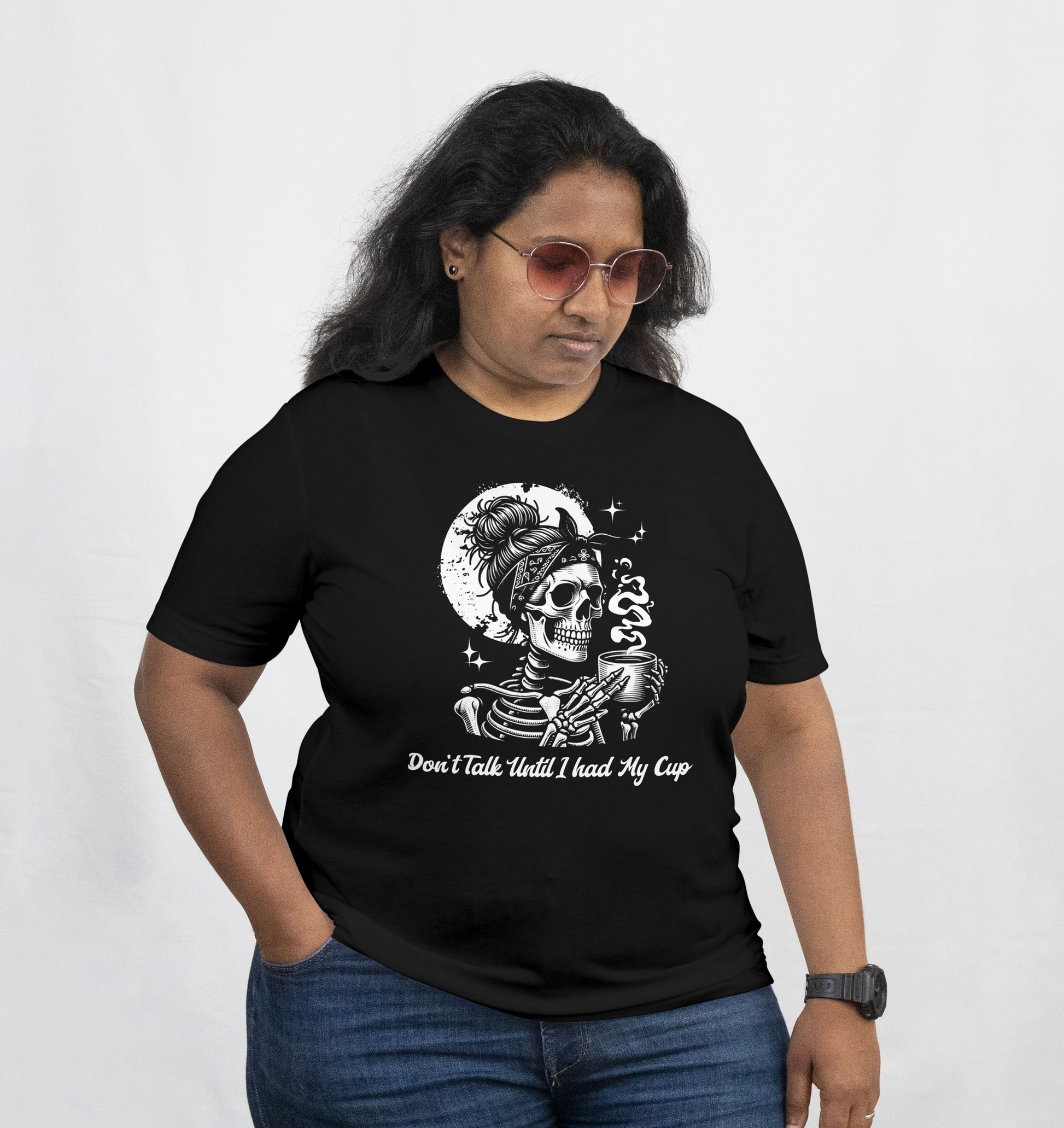 Person wearing a black t-shirt with a skeletal figure with bandana and skeleton hand holding a smoking cup, against a black background with moon and stars. The model is standing  against a white background