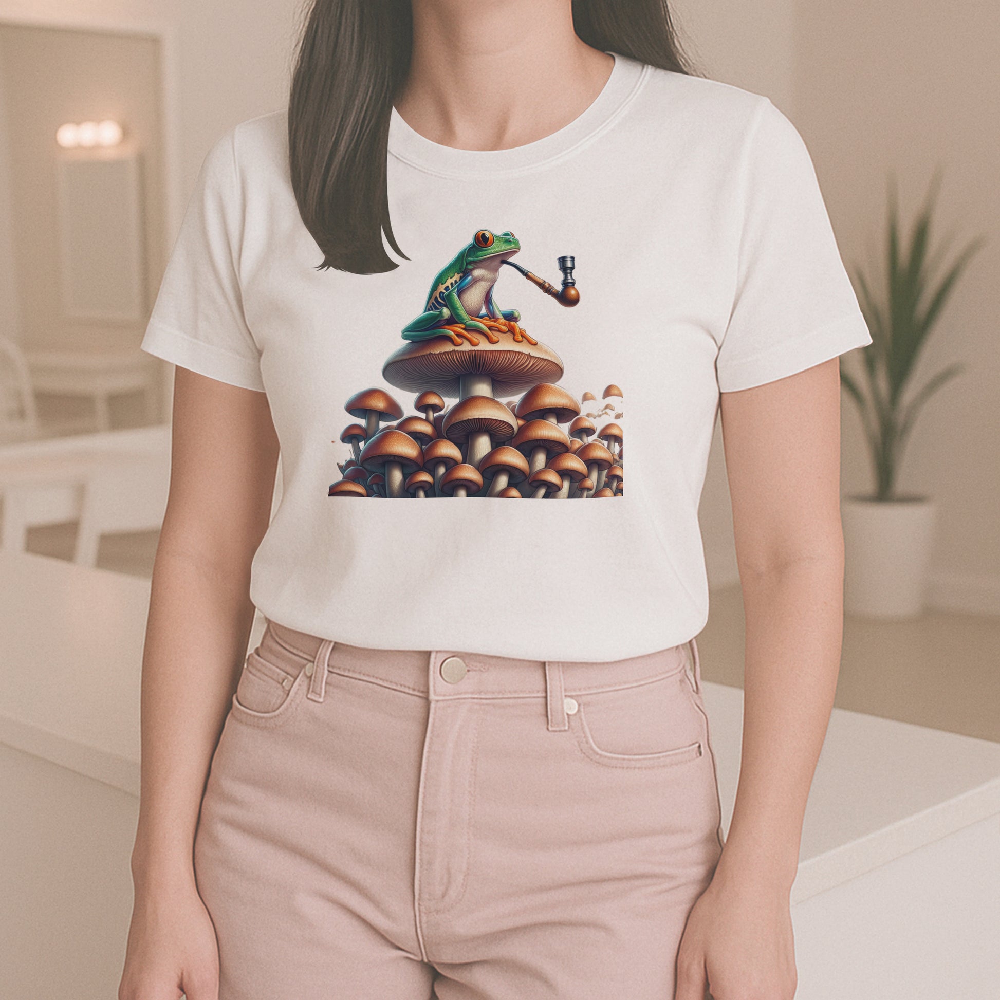 Woman wearing a white t-shirt with a Frog smoking a pipe on a mushroom with more mushrooms in the background. The woman is standing in a well lite room