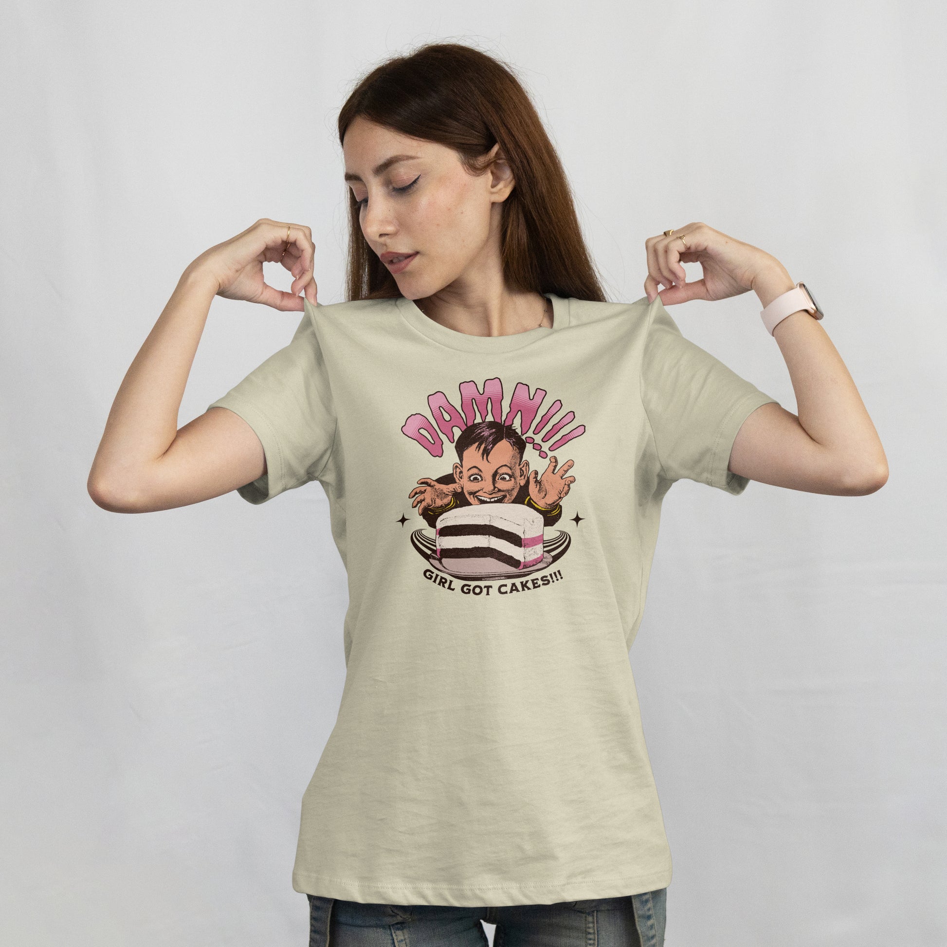 Woman wearing a t shirt with a cartoon character with a cake and text 'Damn!!! Girl Got Cakes!!!' on a white background.